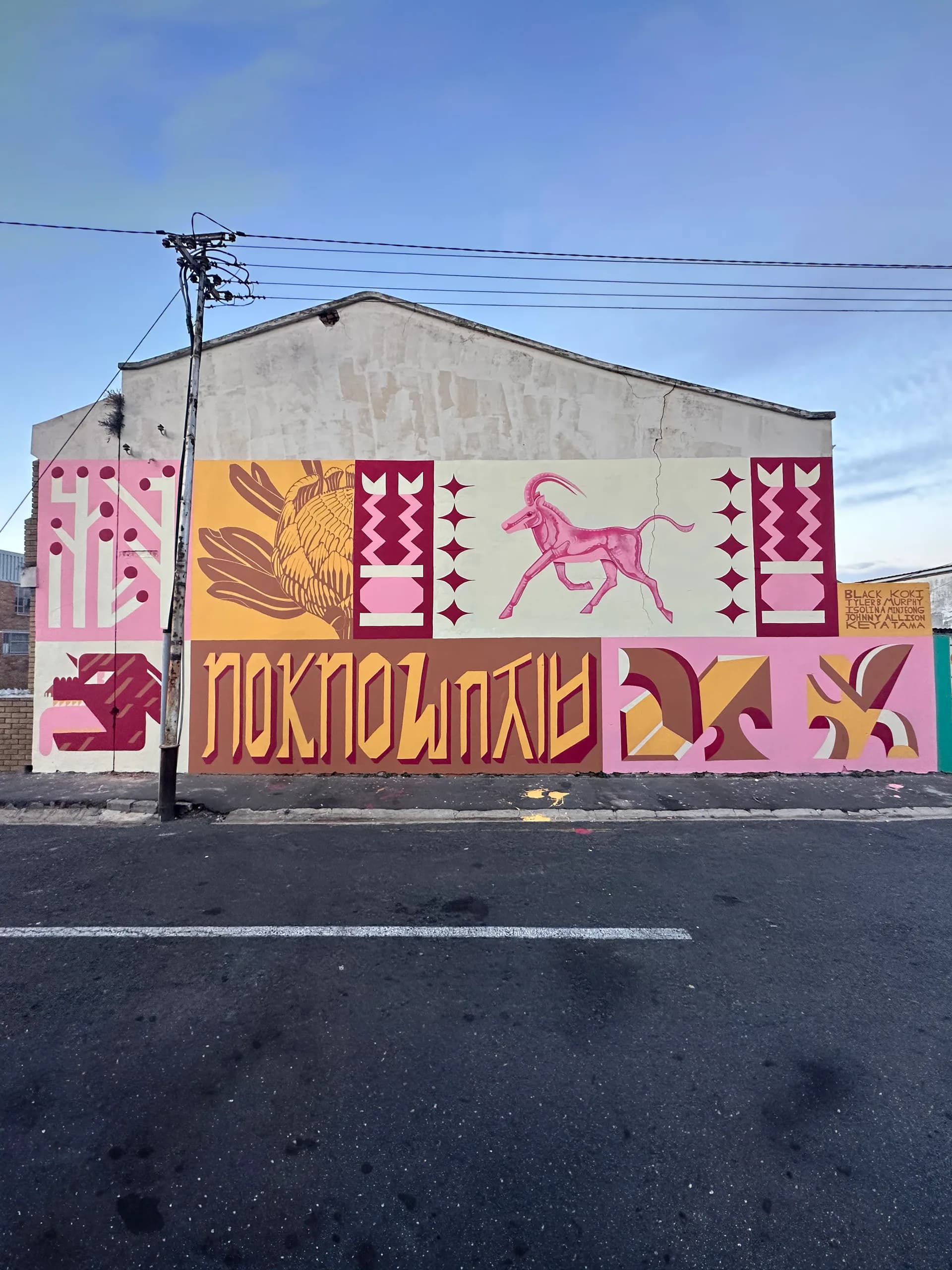 Large outdoor mural on building exterior featuring bold graphic animal and botanical forms in pink, yellow, and burgundy