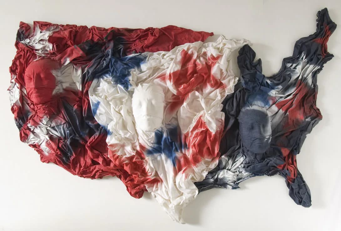 Red, white, and blue crumpled plastic map of the United States mounted on white wall.