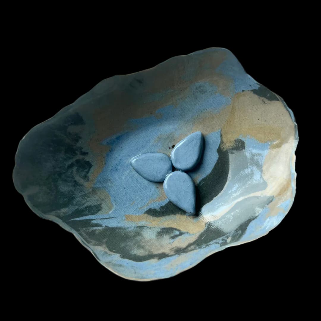 Hand-built ceramic dish with ruffled edges, blue and earth-tone glaze with raised teardrop petal motif at center