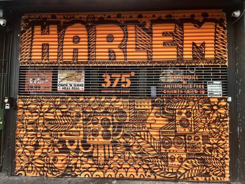 Storefront with orange and black corrugated metal shutter featuring intricate geometric and figurative line-art patterns.