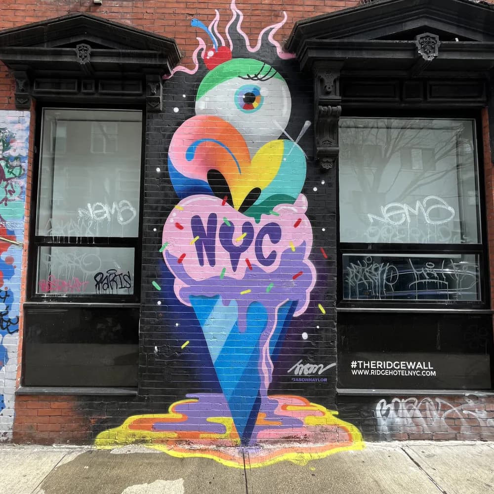 Colorful mural of an ice cream cone character with a large eye, open mouth, pink brain, and 'NYC' text on the cone, painted on storefront by Jason Naylor.