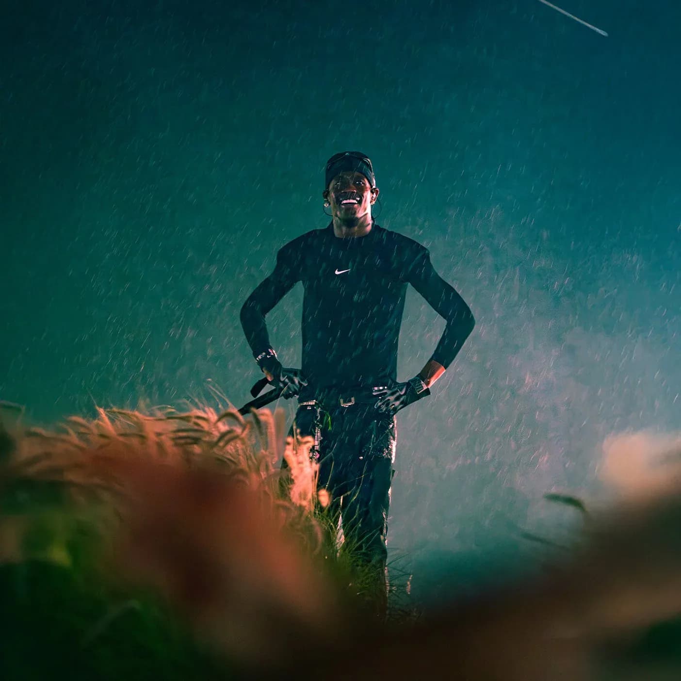 Athlete in black Nike gear standing with hands on hips against teal and orange gradient background with bokeh lights.