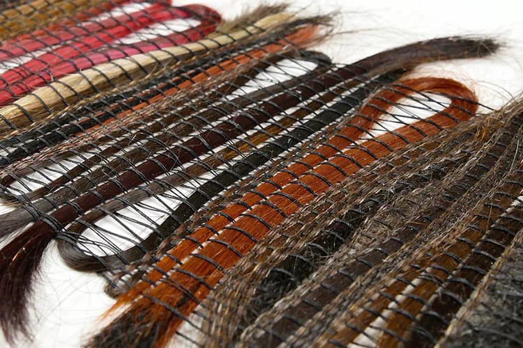 Woven textile strips in red, black, orange, and brown with exposed hair fibers, arranged diagonally on white background.