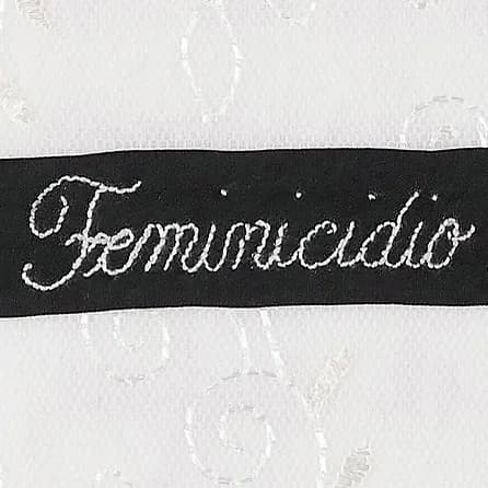 Black fabric band with white embroidered script text reading 'Femminucidio' on textured white background.