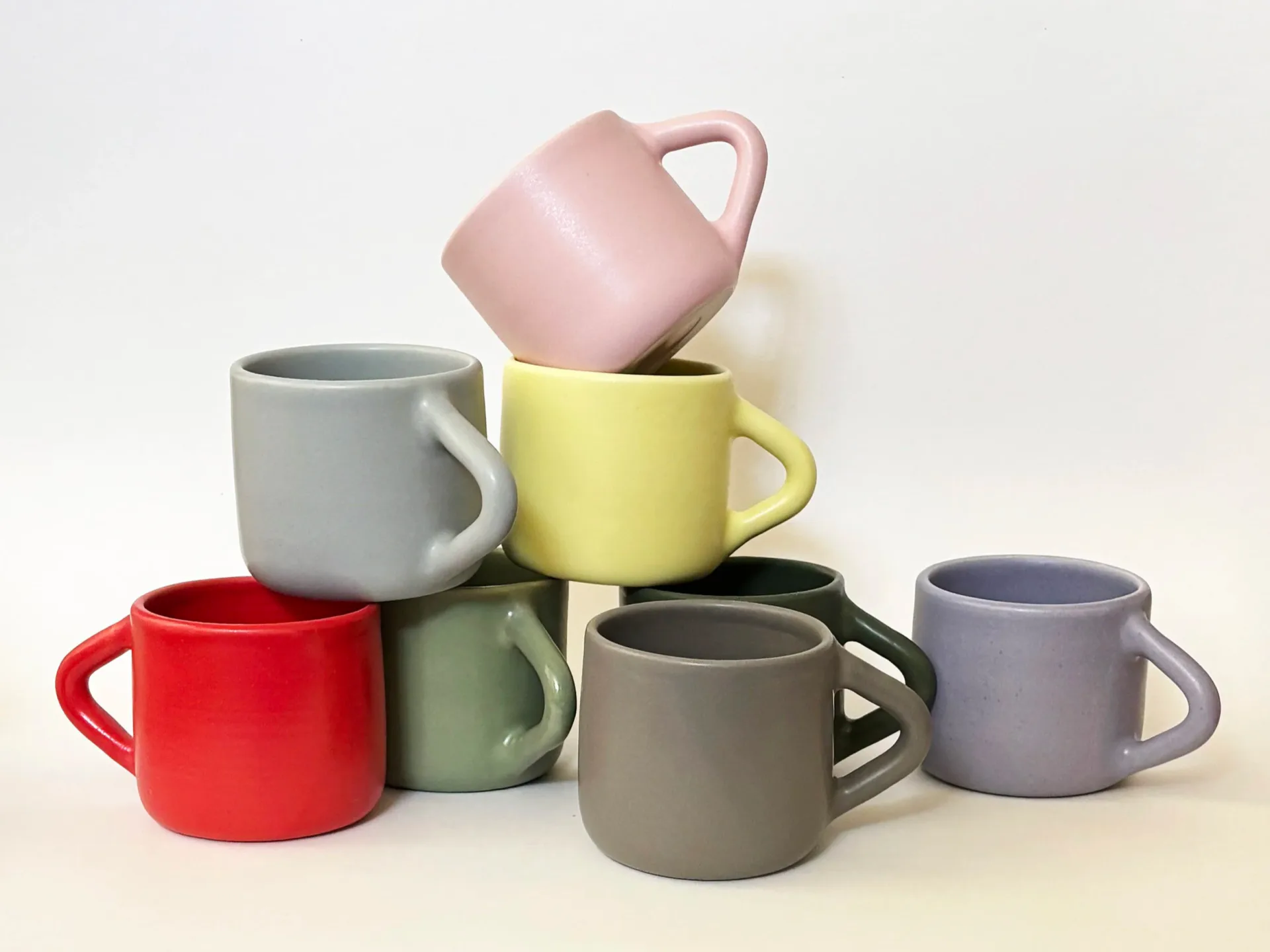 Stacked ceramic mugs in muted colors—gray, yellow, pink, red, green, and lavender—by Joanne Lee.