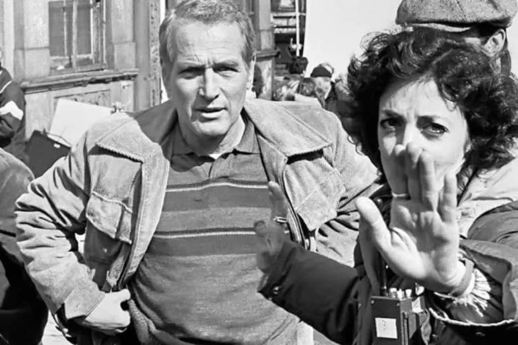 Black and white photograph by Joe Conzo, Jr. of two men on an urban street; one gestures while speaking to the other in what appears to be a candid documentary moment from the 1970s.
