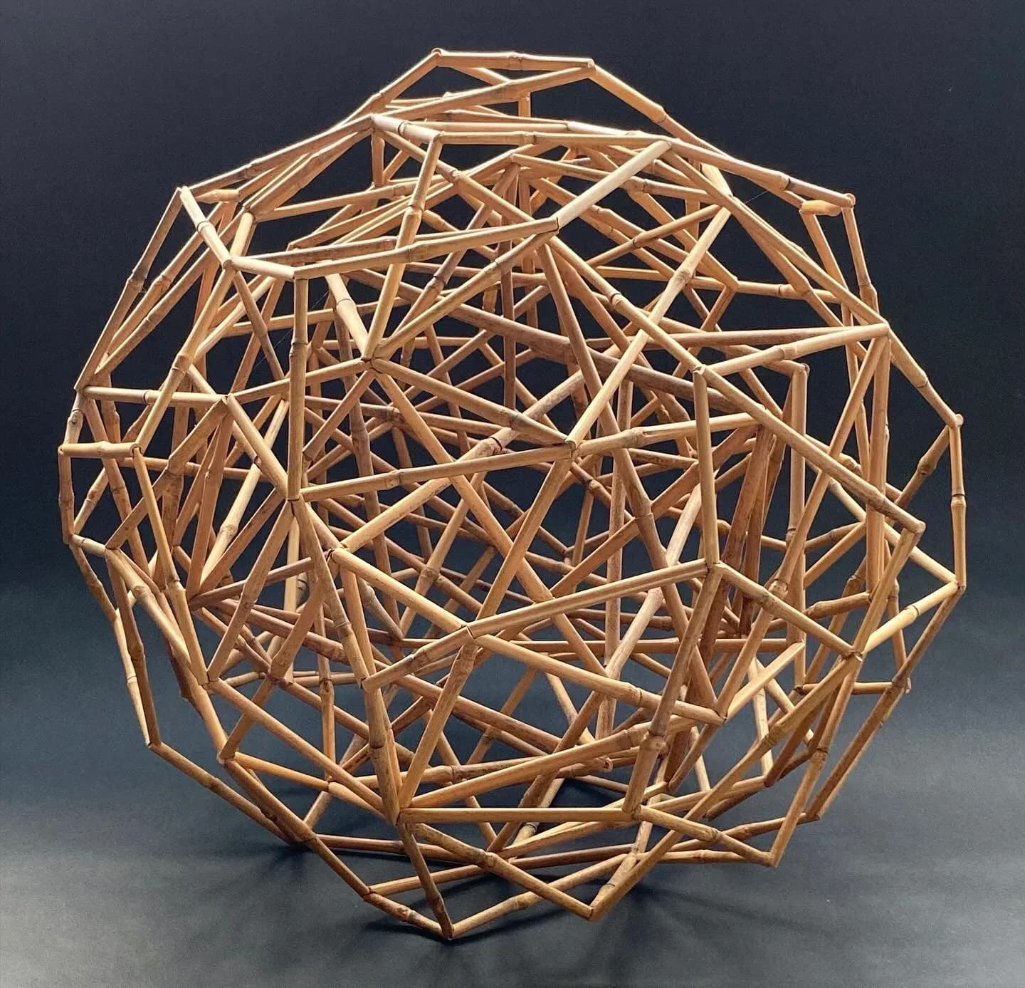 Geometric bamboo lattice sphere sculpture with triangular panels against gray background