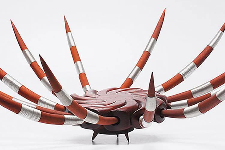 Sculptural piece by Josué Guarionex featuring a spiky wooden base with long spindle-like spikes wrapped in orange and silver bands radiating outward like spider legs