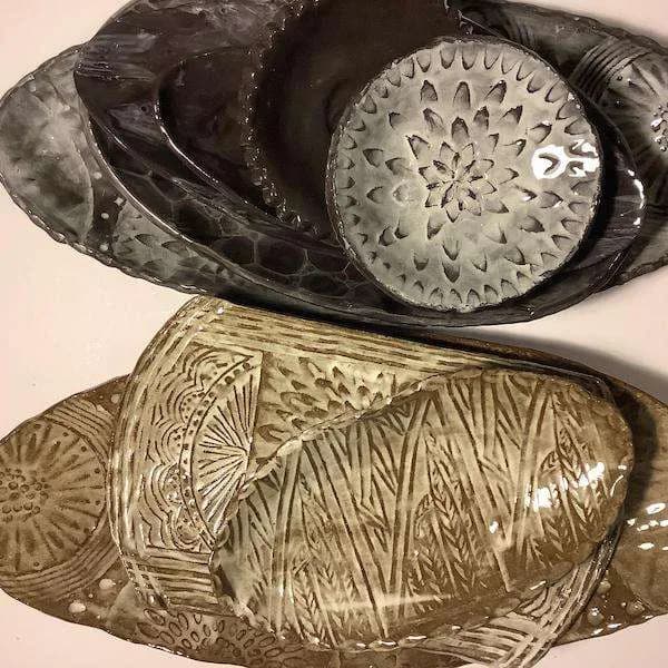 Two ceramic vessels with carved geometric circular and linear patterns; one in black glaze, one in cream with detailed surface work.