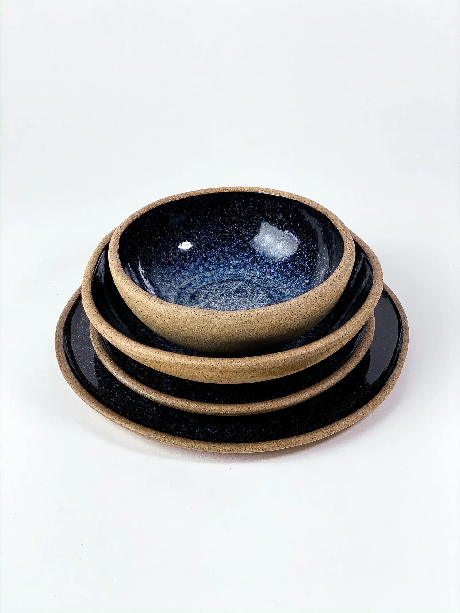 Stacked ceramic dinnerware set with sandy stoneware exterior and deep navy/black galaxy glaze interior