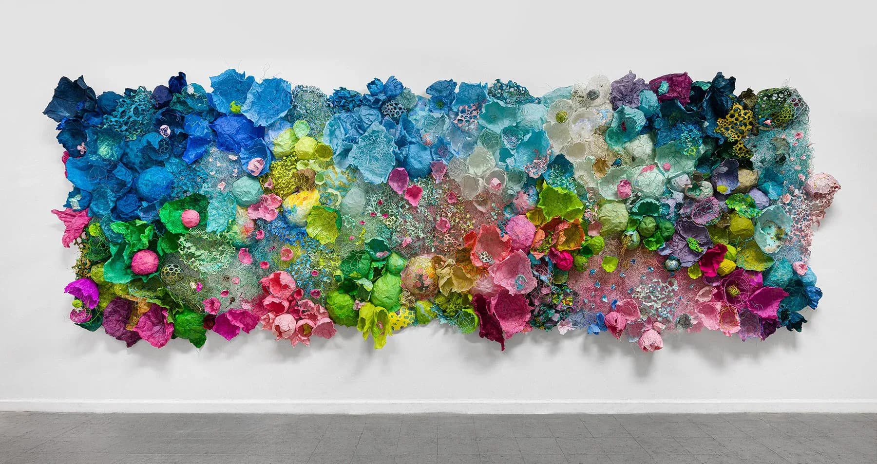 Large-scale colorful paper sculptural wall installation with floral and coral forms in blues, pinks, and greens