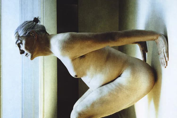 Nude male figure in crouched pose against white wall with geometric shadows, photograph by Kari Soinio.