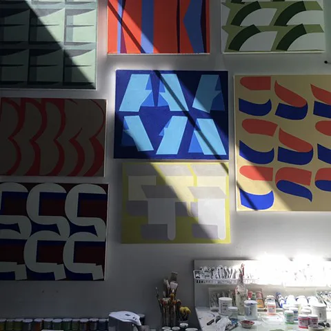 Studio wall with multiple geometric abstract paintings in bold colors including red, blue, green, and yellow