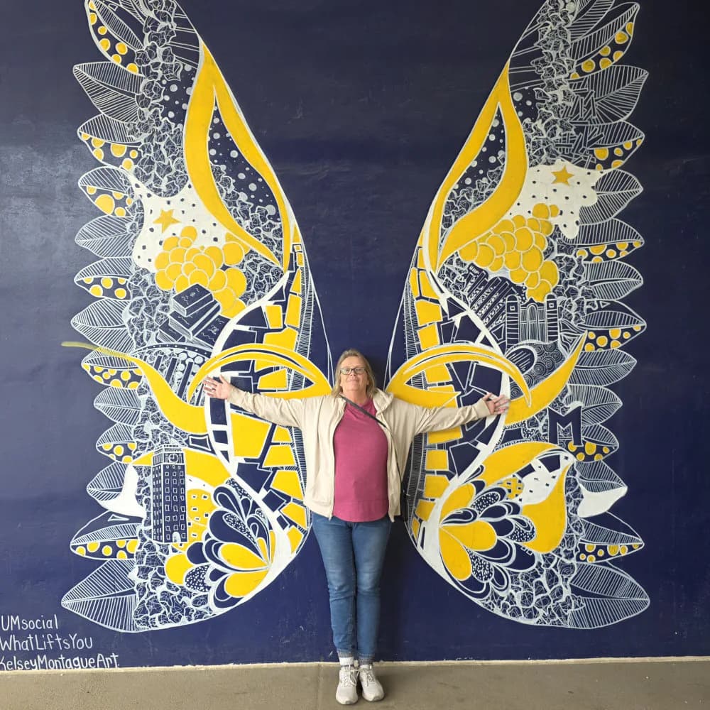 Mural on dark blue wall depicting two large ornate butterfly wings in yellow, white, and gray with intricate line work and detailed patterning throughout both wings.