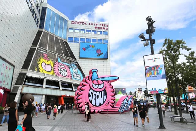 Large-scale inflatable sculpture of a pink cartoon character with 'Seoul' text installed in front of Doota Duty Free building