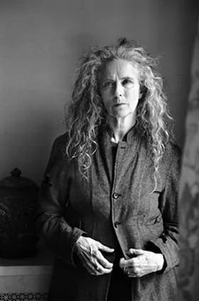 Black and white portrait photograph of a woman with long curly hair, wearing a cardigan, looking directly at camera.