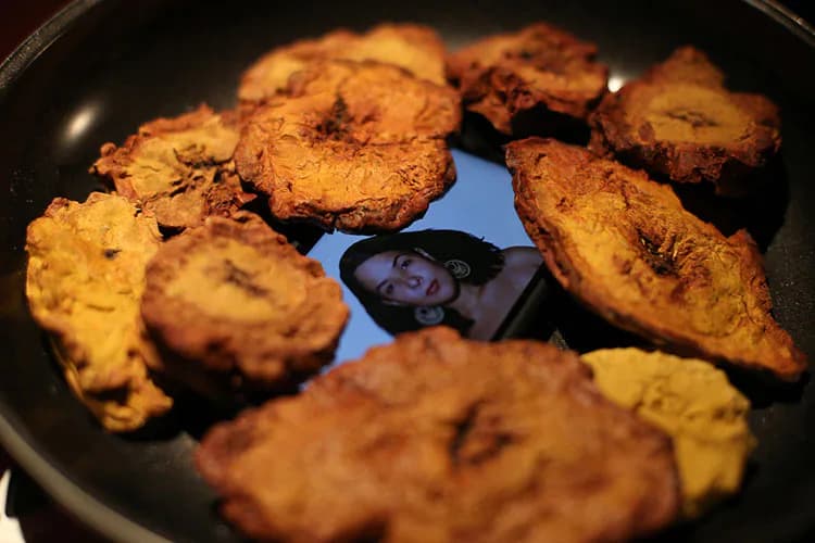 Golden-brown fried plantain chips arranged in a dark pan with a blue reflection visible in the center.