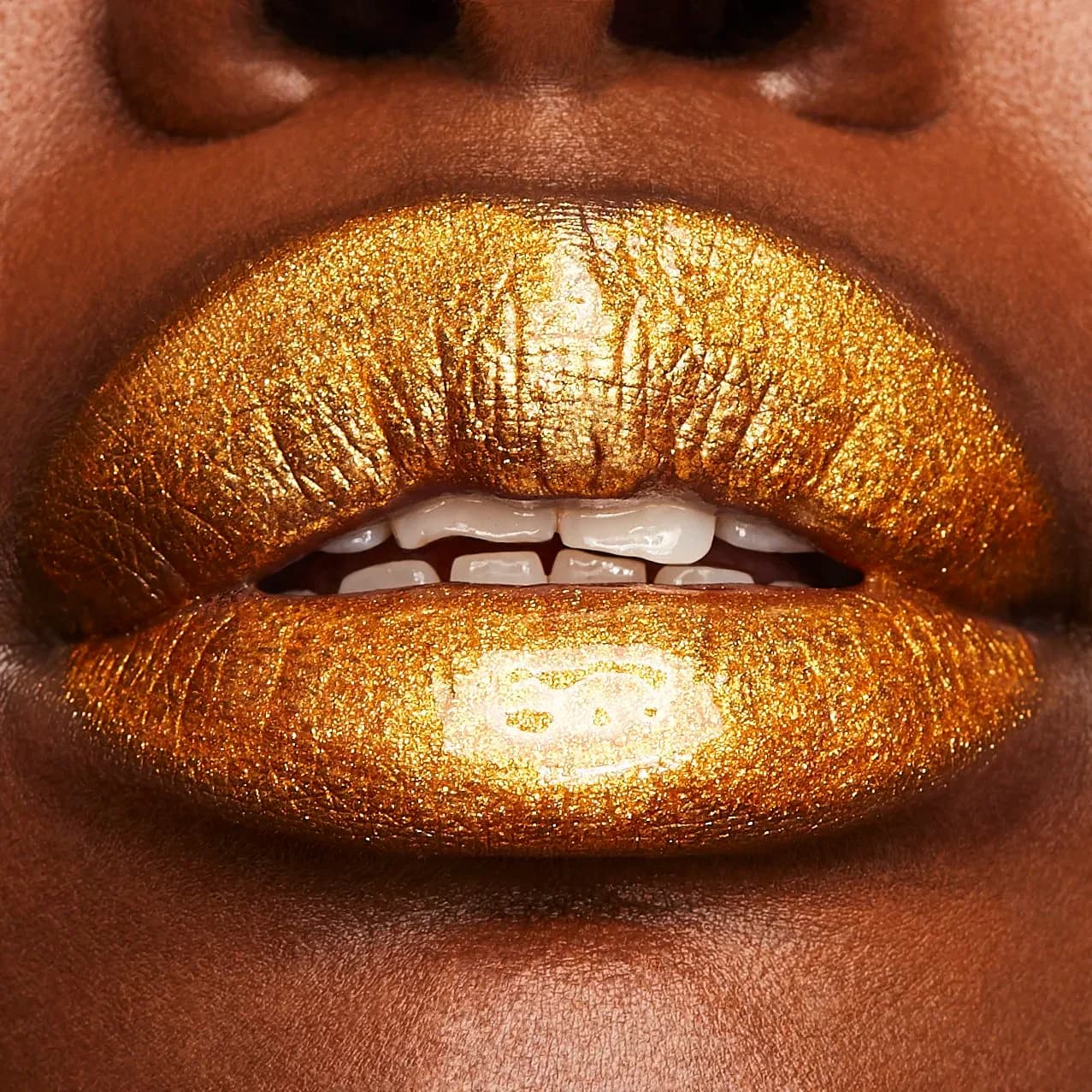 Close-up of lips covered in gold metallic makeup with subtle symbol