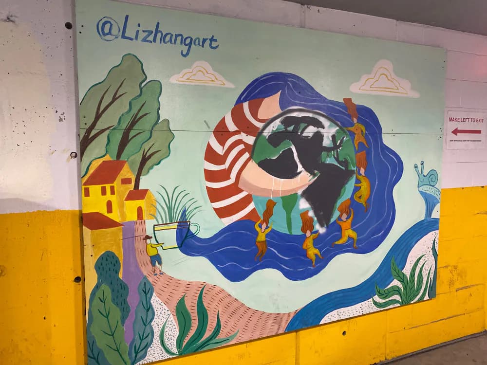 Colorful mural by Li Zhang featuring a figure with blue hair in a striped shirt emerging from swirling blue water, with yellow house and green plants in mixed-media style.