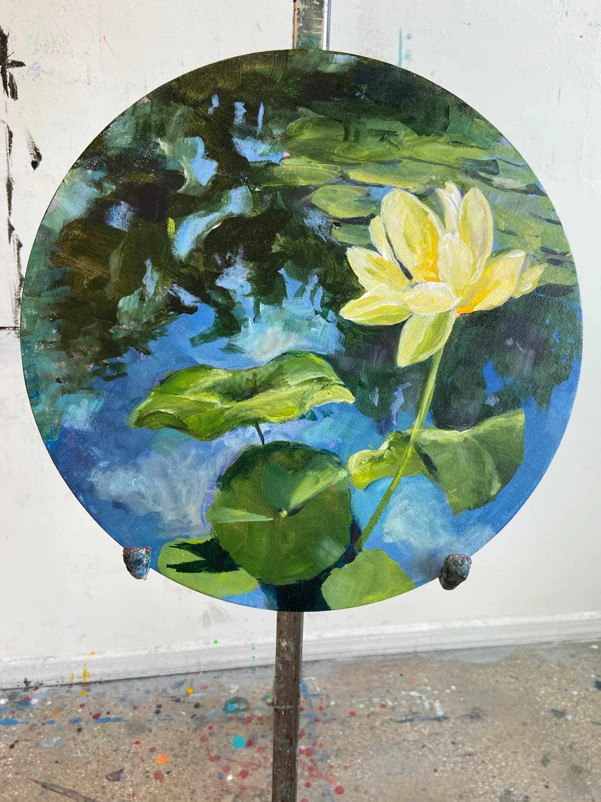 Round tondo painting of a yellow water lily with lily pads on reflective blue pond water
