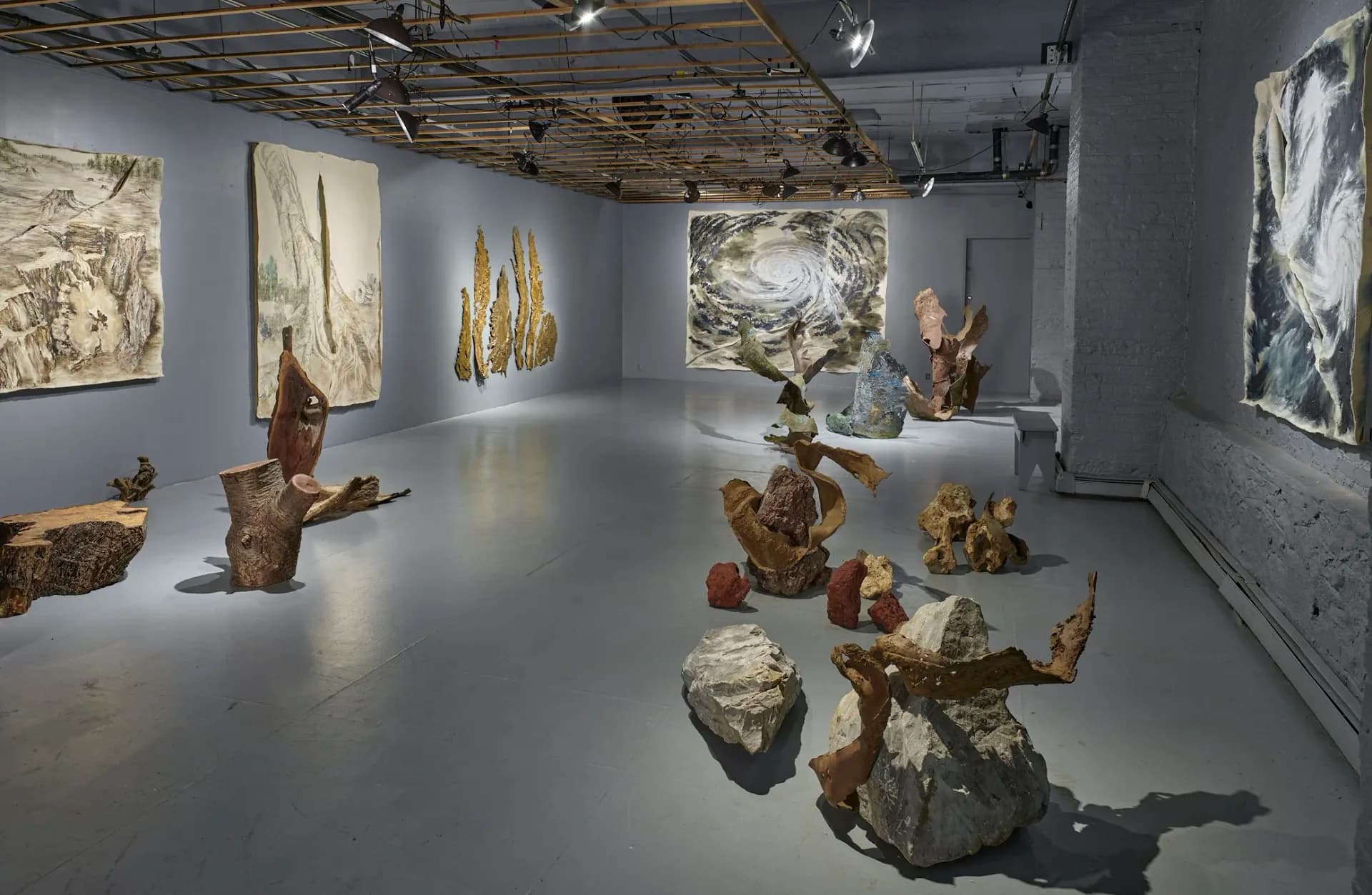 Gallery interior with polished concrete floor displaying sculptural works and wall-mounted drawings in warm and neutral tones.
