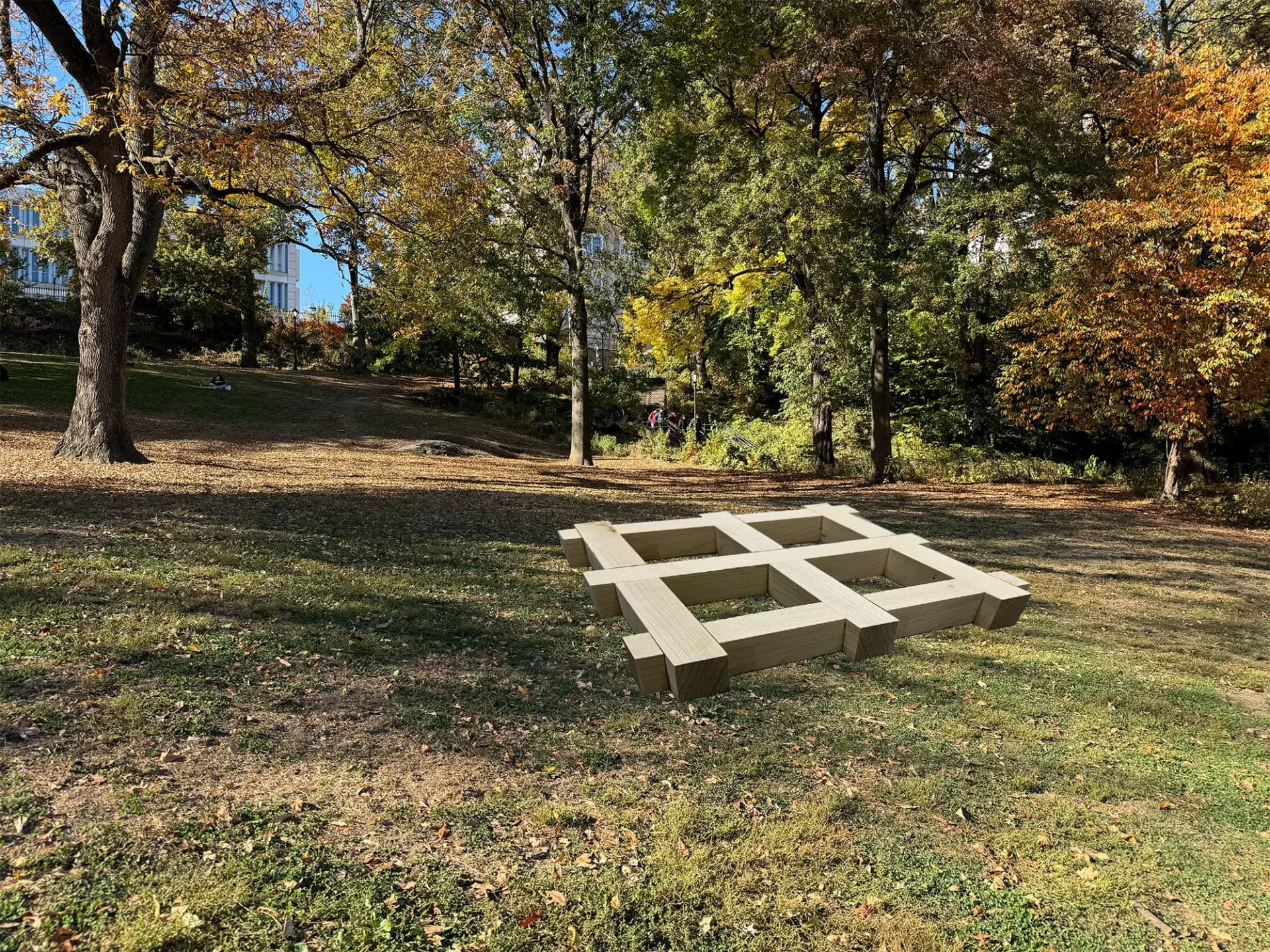 Large-scale geometric wooden installation on grass in an autumn park setting