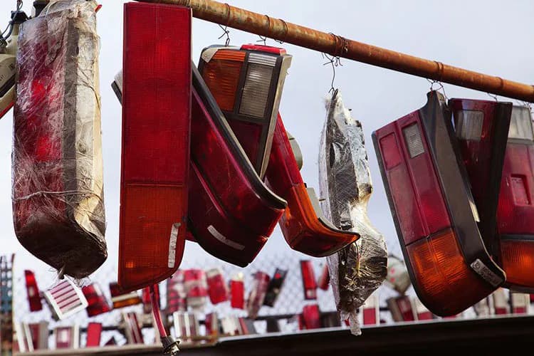 Red and burgundy fabric panels hanging from a rope, weathered and textured, suspended over an outdoor space with blurred figures below.