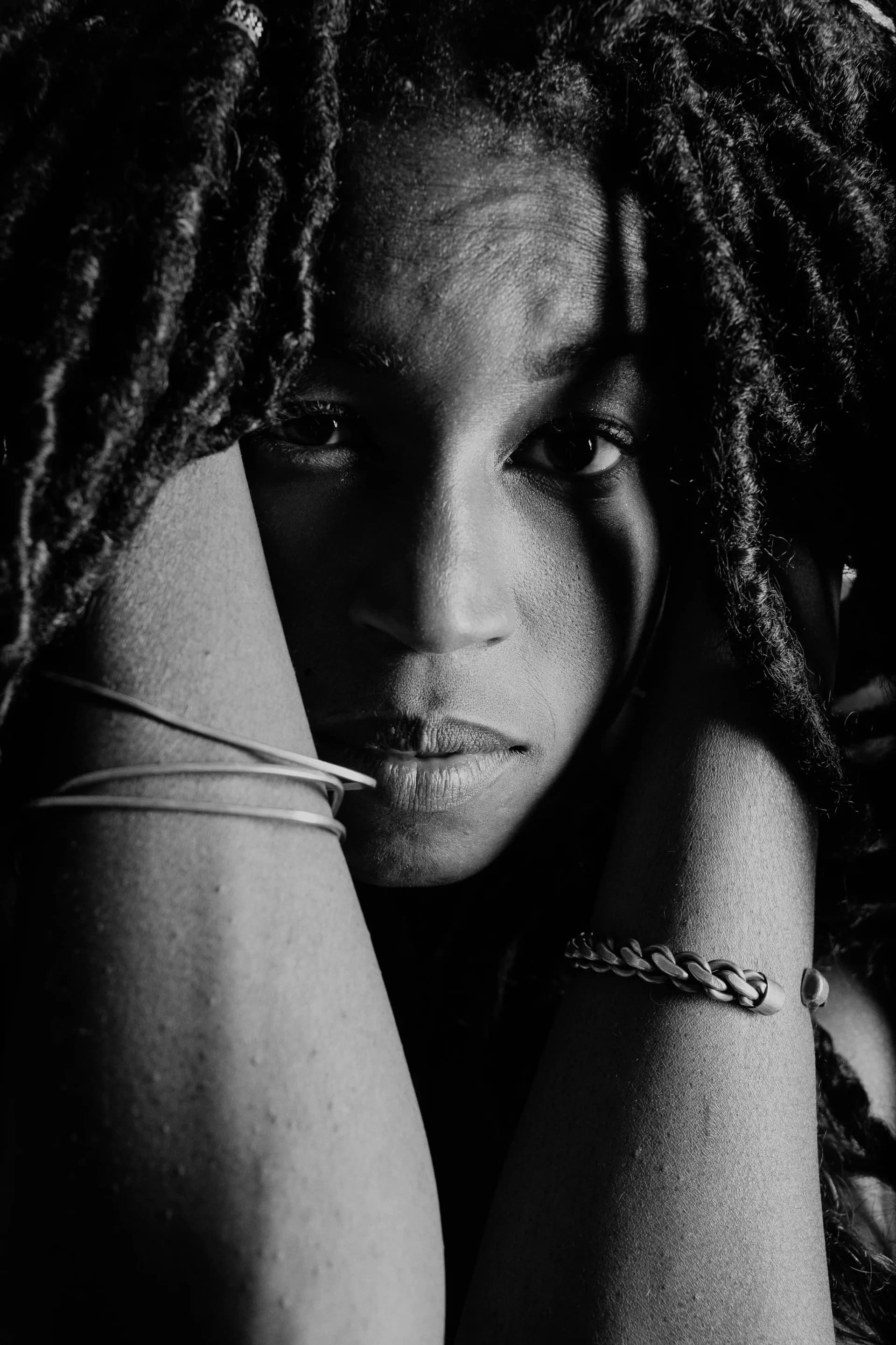 Black and white close-up portrait with dramatic shadow lighting of subject with dreadlocks and bracelets