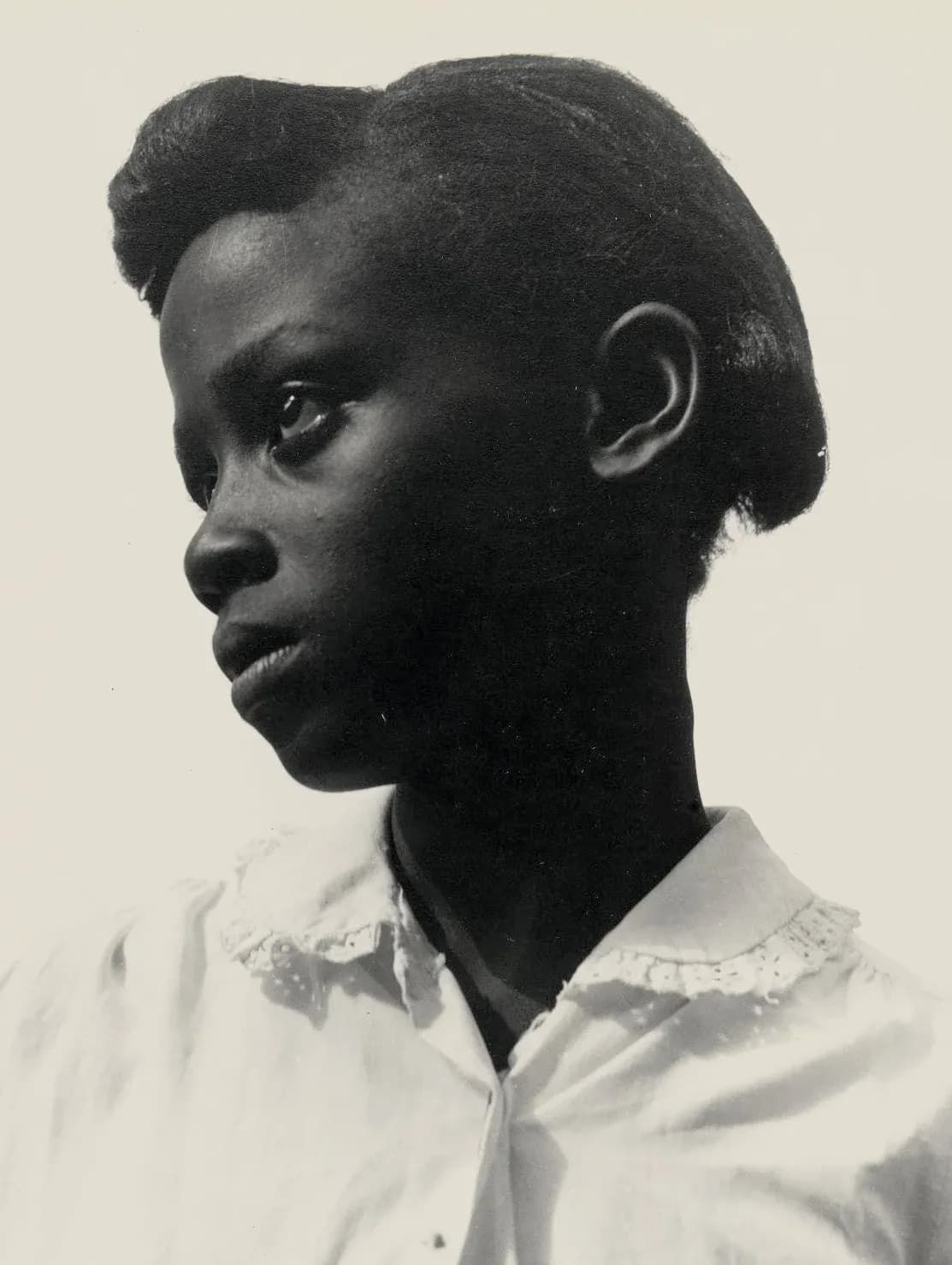 Black and white portrait of a young woman in profile against a plain background, wearing a white lace-collared blouse