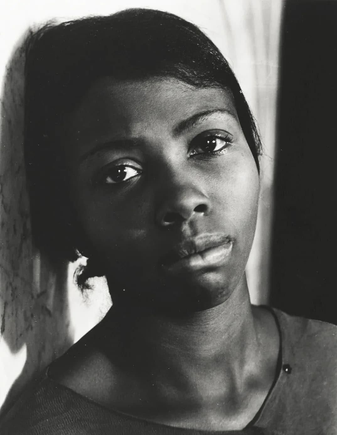 Black and white close-up portrait of a young Black woman with dramatic side lighting against a textured wall