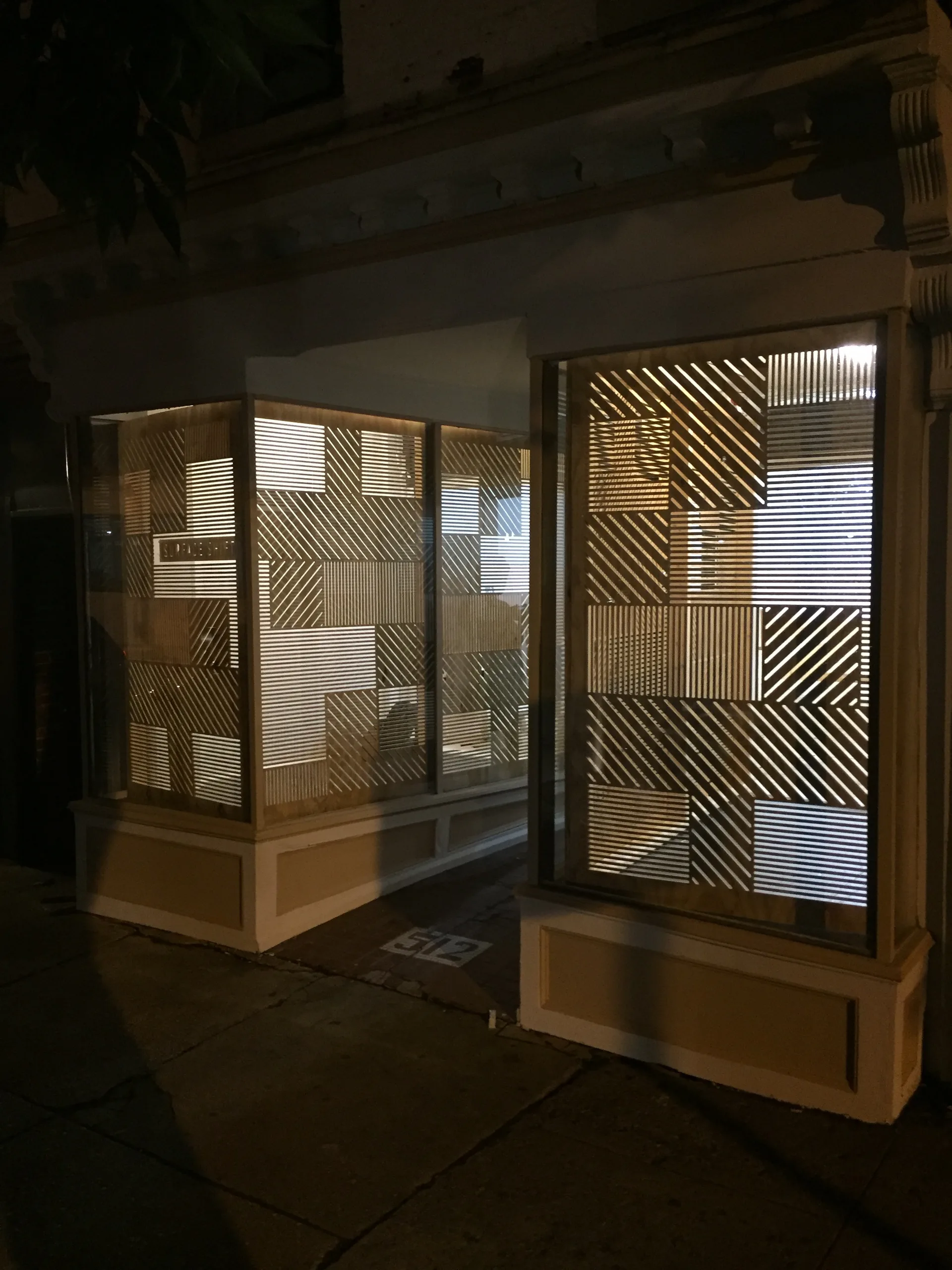 Illuminated geometric laser-cut wood panels in gallery windows at night