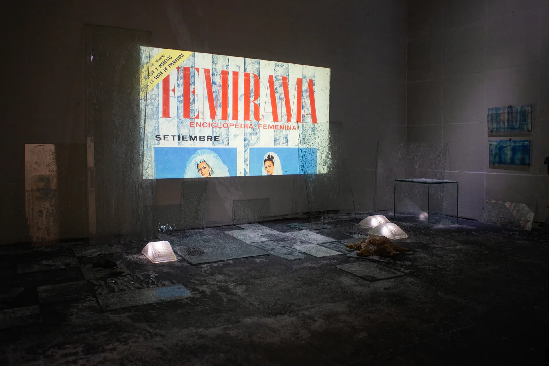 Large-scale immersive installation with Femirama projection, glass elements, and scattered objects on dark floor