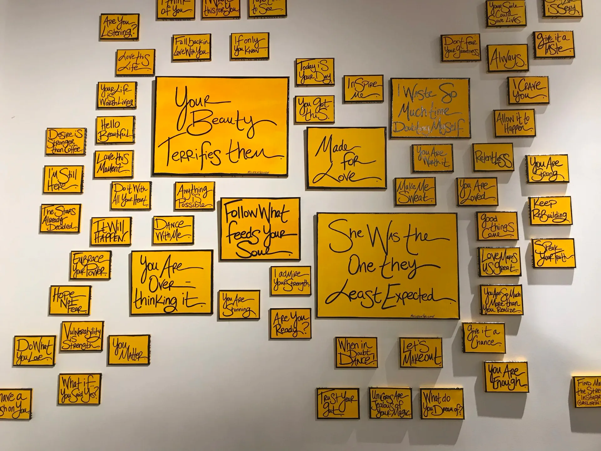 Wall installation of dozens of yellow painted canvases with handwritten text messages