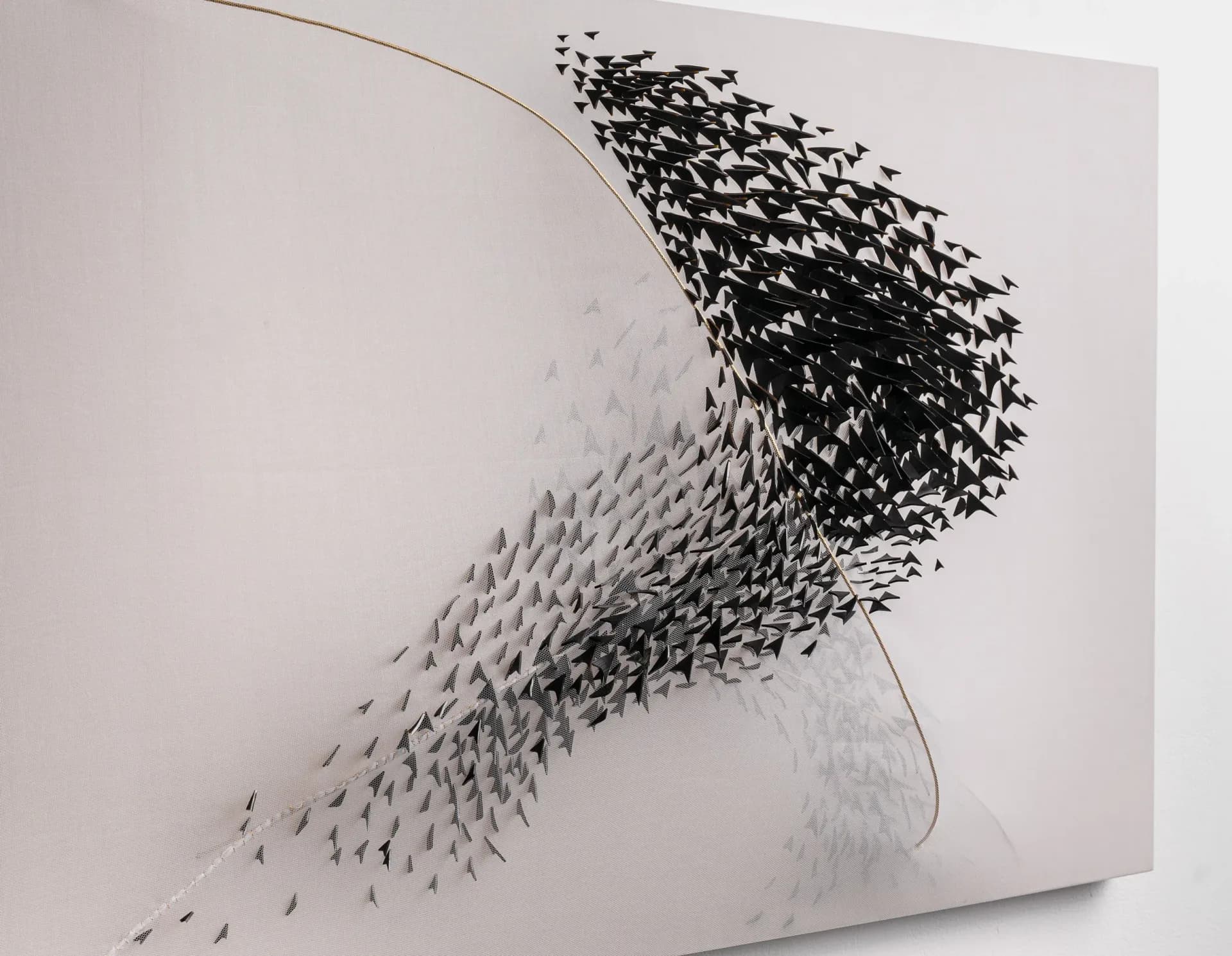 Large wall installation with hundreds of small black bird-like forms creating a sweeping murmuration pattern on a pale canvas with gold line