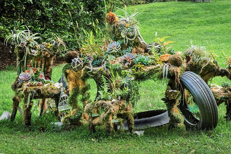 Mixed-media sculpture installation with organic moss-covered forms and found objects including tires on grass, by Natalie Collette Wood.
