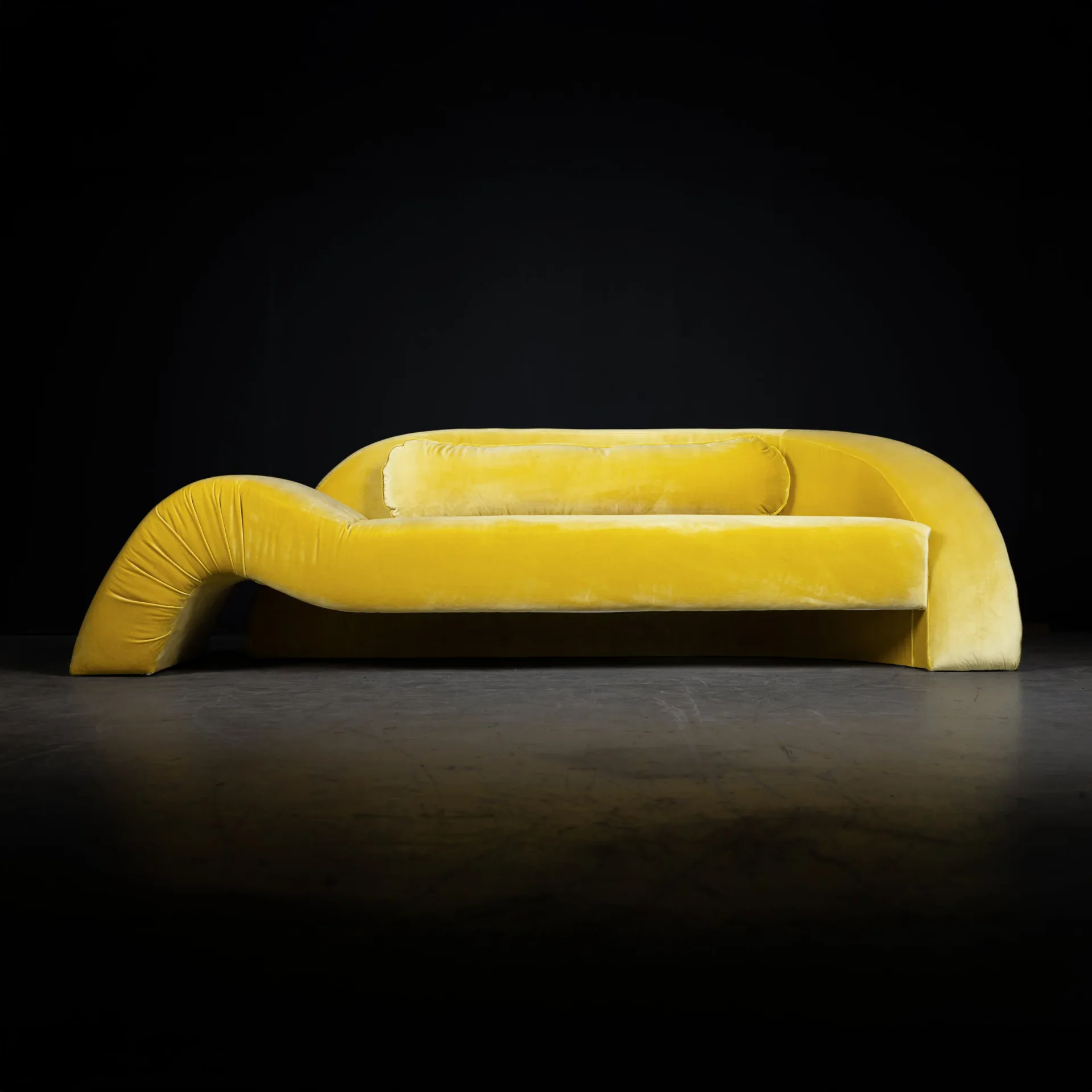 Aeon Sofa in yellow velvet with dramatic curved arm sweeping to the floor, against black background