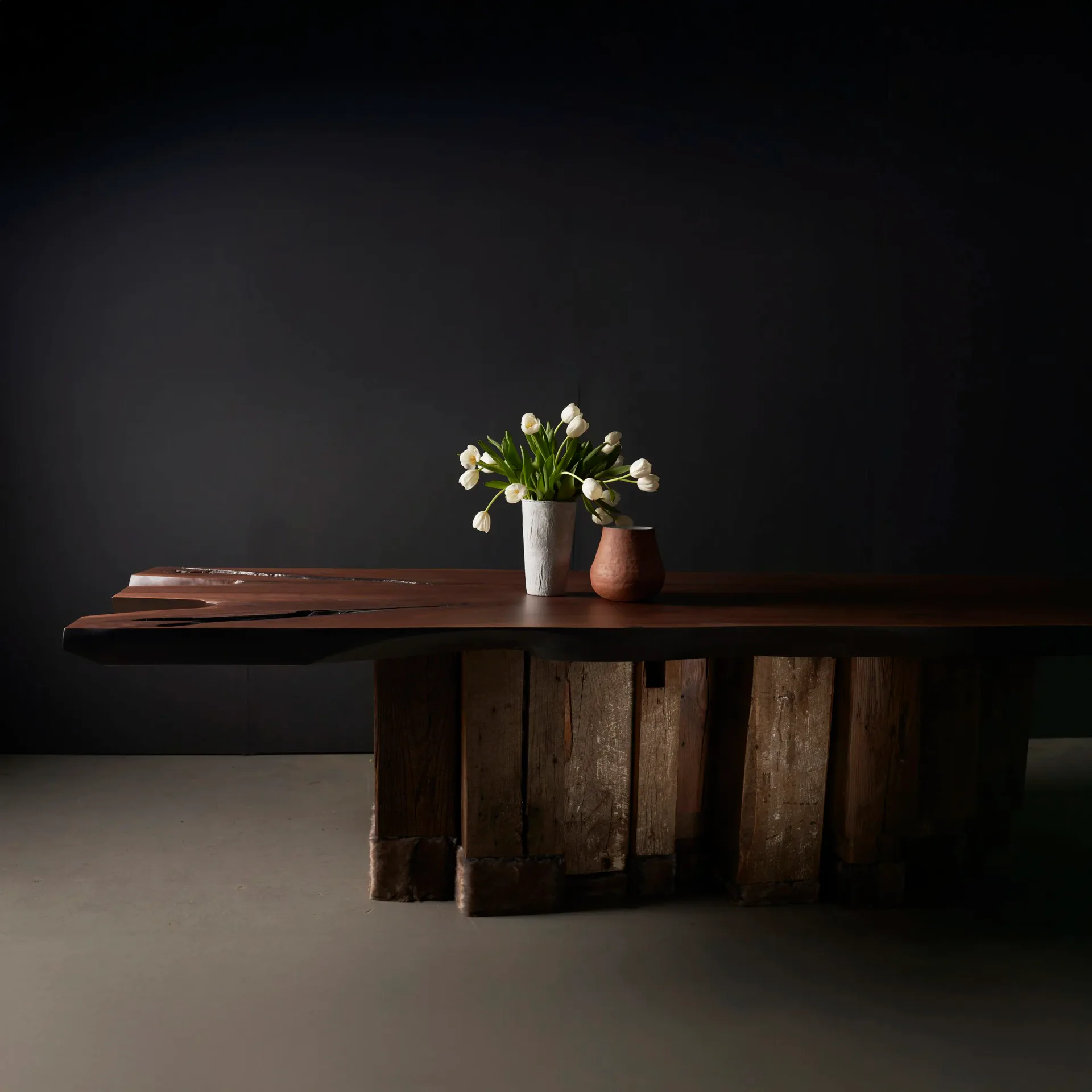 Evolution dining table with dark walnut live-edge top on reclaimed wood beam base, styled with white tulips