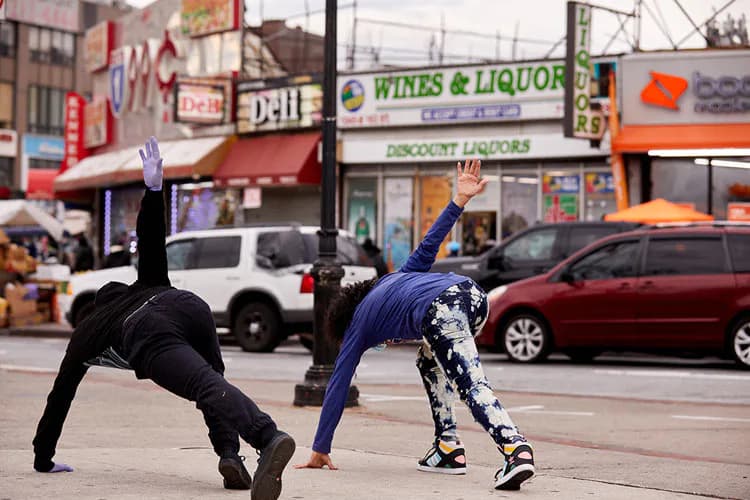 Three figures in dynamic yoga/stretching poses on an urban street, rendered in black and patterned clothing against a city backdrop with storefronts.