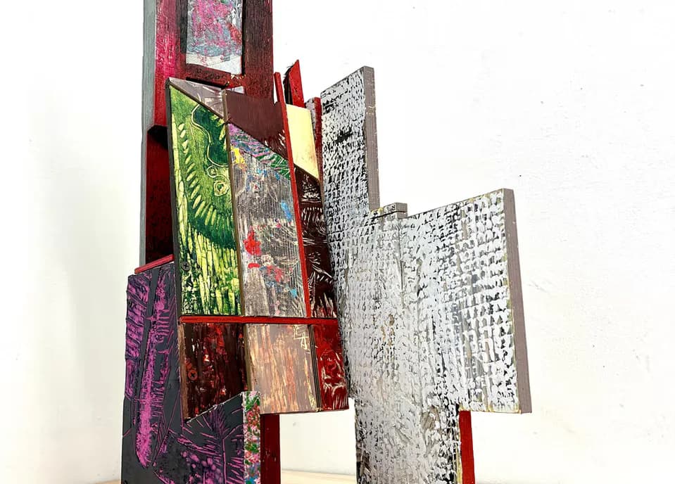 Mixed media sculptural assemblage of painted wood panels in red, green, and silver tones against white wall