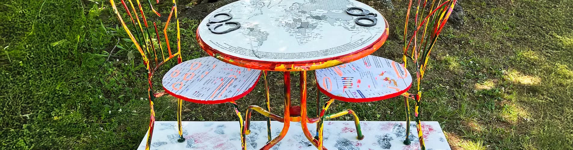 Colorful mixed-media installation of painted table and chairs with world map and text elements, photographed outdoors