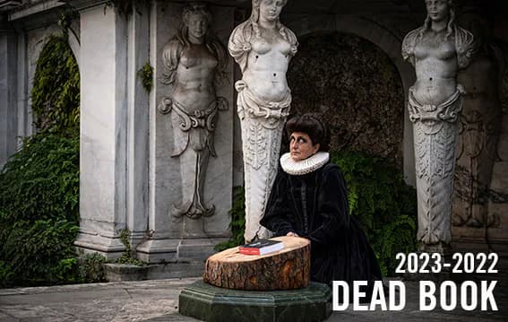 Person in Renaissance-style collar seated at tree stump before classical stone statues with ivy; titled 'Dead Book 2023-2022'.