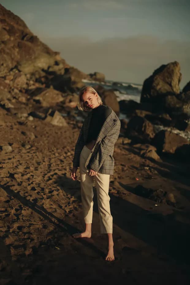 Fashion portrait of a woman in plaid blazer on rocky beach at golden hour