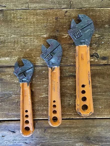 Three orange-handled adjustable wrenches arranged on wood background