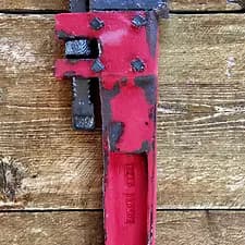 Red and black pipe wrench mounted vertically on wooden background