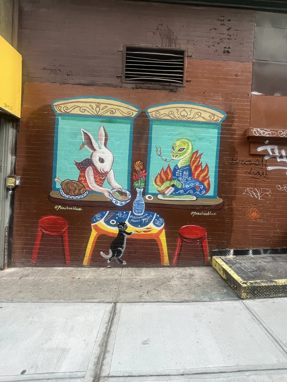 Mural on brick wall depicting a white rabbit and figure with flames at a table with red chairs, turquoise and warm tones, signed Peach Tao.