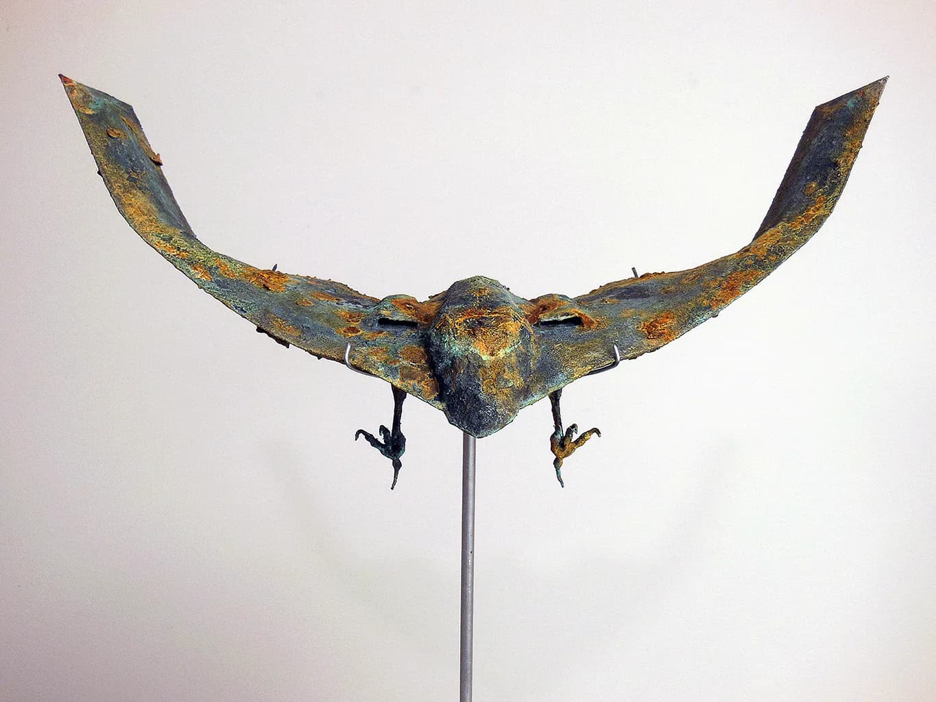 Bronze bird sculpture with wide wings mounted on a metal rod, verdigris patina