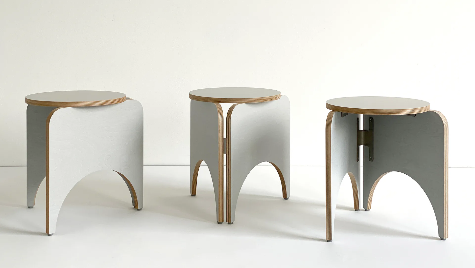 Three grey and birch plywood stools with arched legs in various configurations