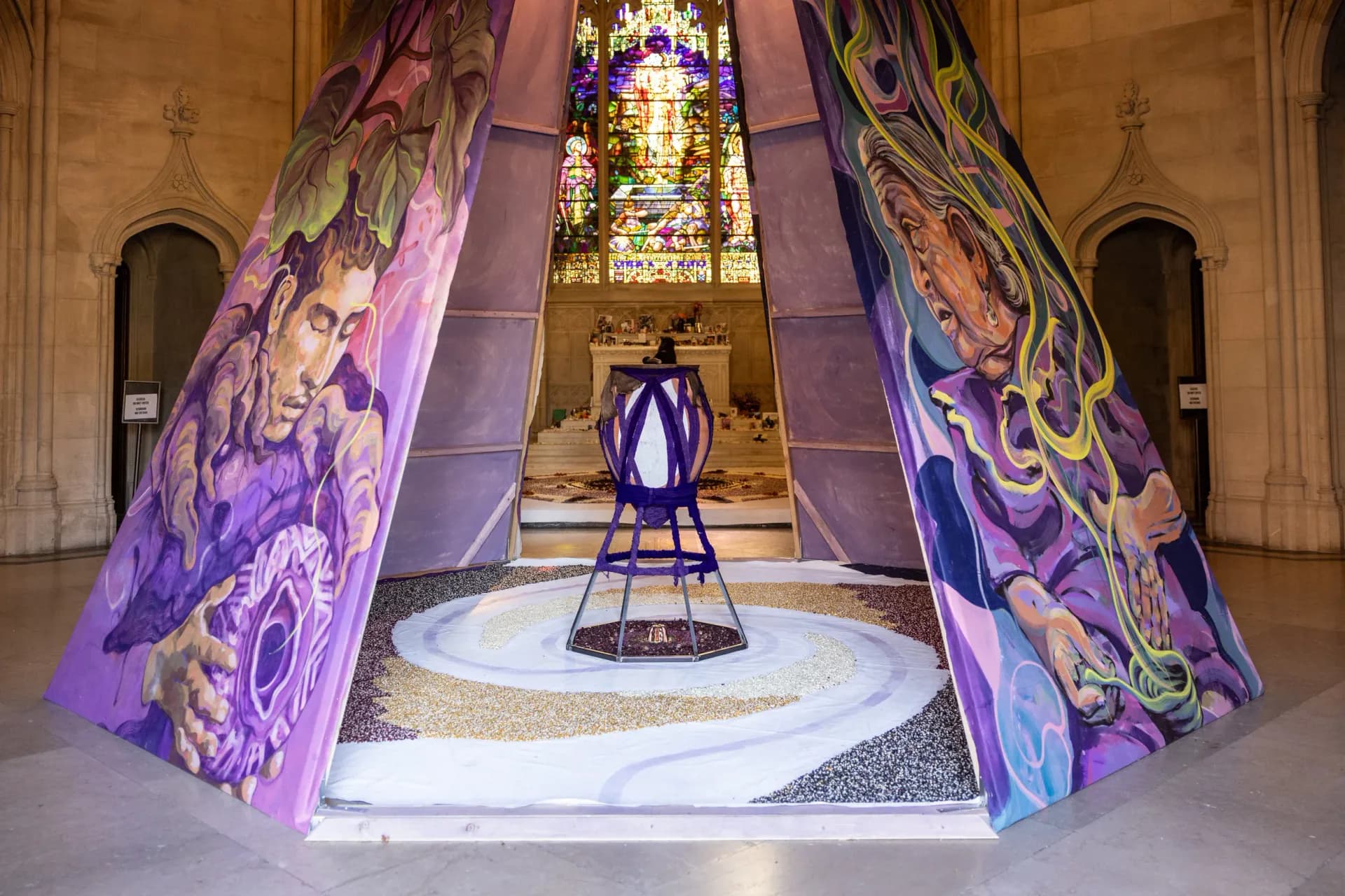 Close-up interior view of painted purple installation panels featuring figurative imagery with stained glass window visible through the opening