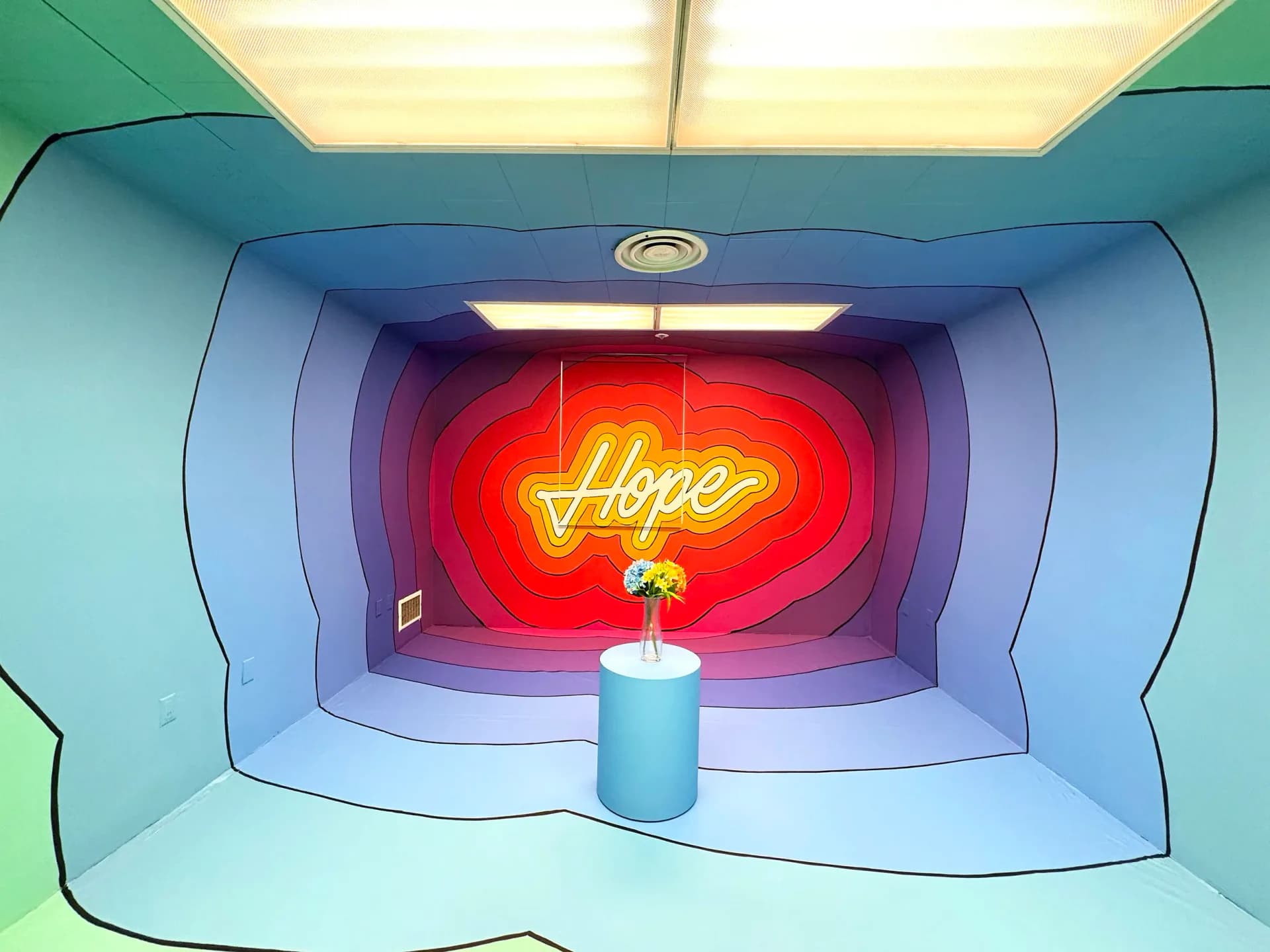 Neon sign installation in alcove displaying red and yellow cursive 'Hope' text against soft blue and green wall.