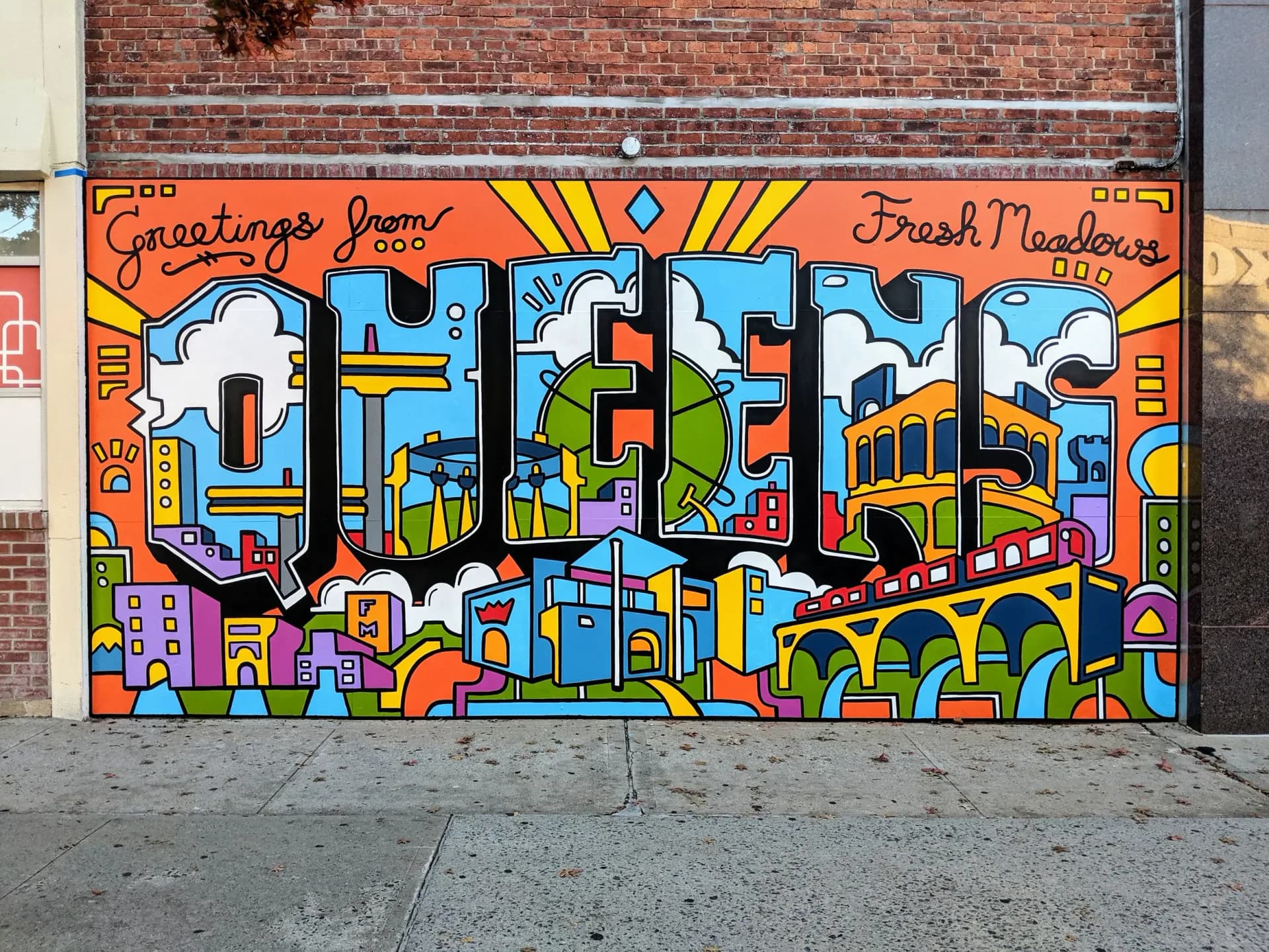 Large-scale mural on brick featuring 'GREENE' in bold blue letters surrounded by colorful geometric patterns, cityscapes, and 'Greetings from Fresh Meadows' text.